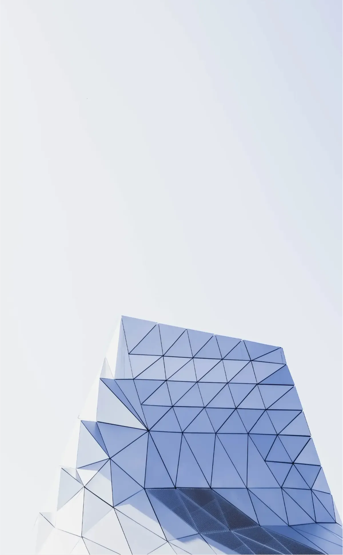 Faceted triangular glass panels at the top of a modern building against a pale sky