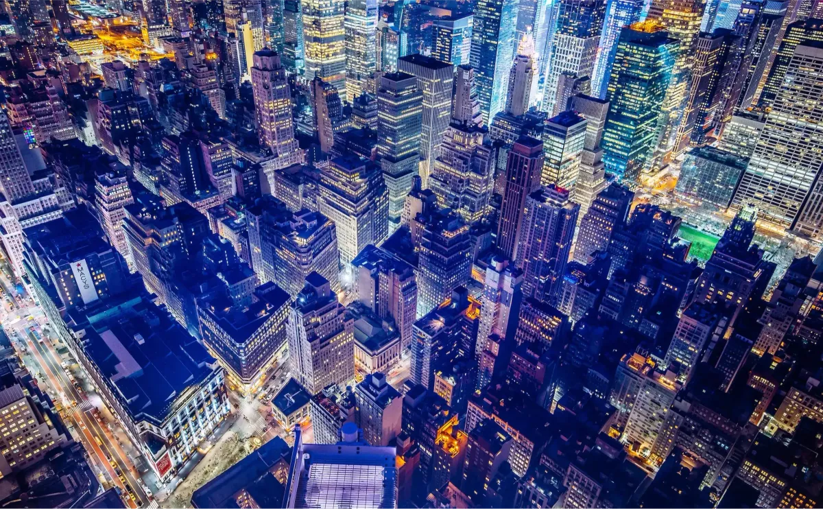 A dense city grid photographed from directly above at night, thousands of lit buildings and intersecting streets extending to every edge of the frame.