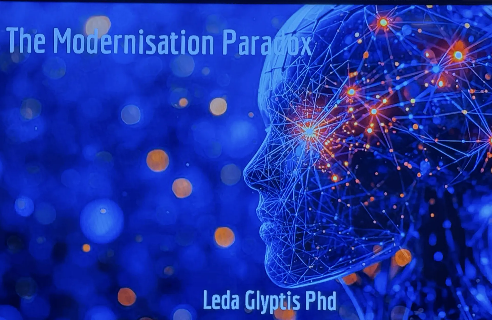 Diapositiva de título con el texto The Modernisation Paradox, Leda Glyptis PhD, sobre la ilustración de una cabeza humana dibujada como una red luminosa