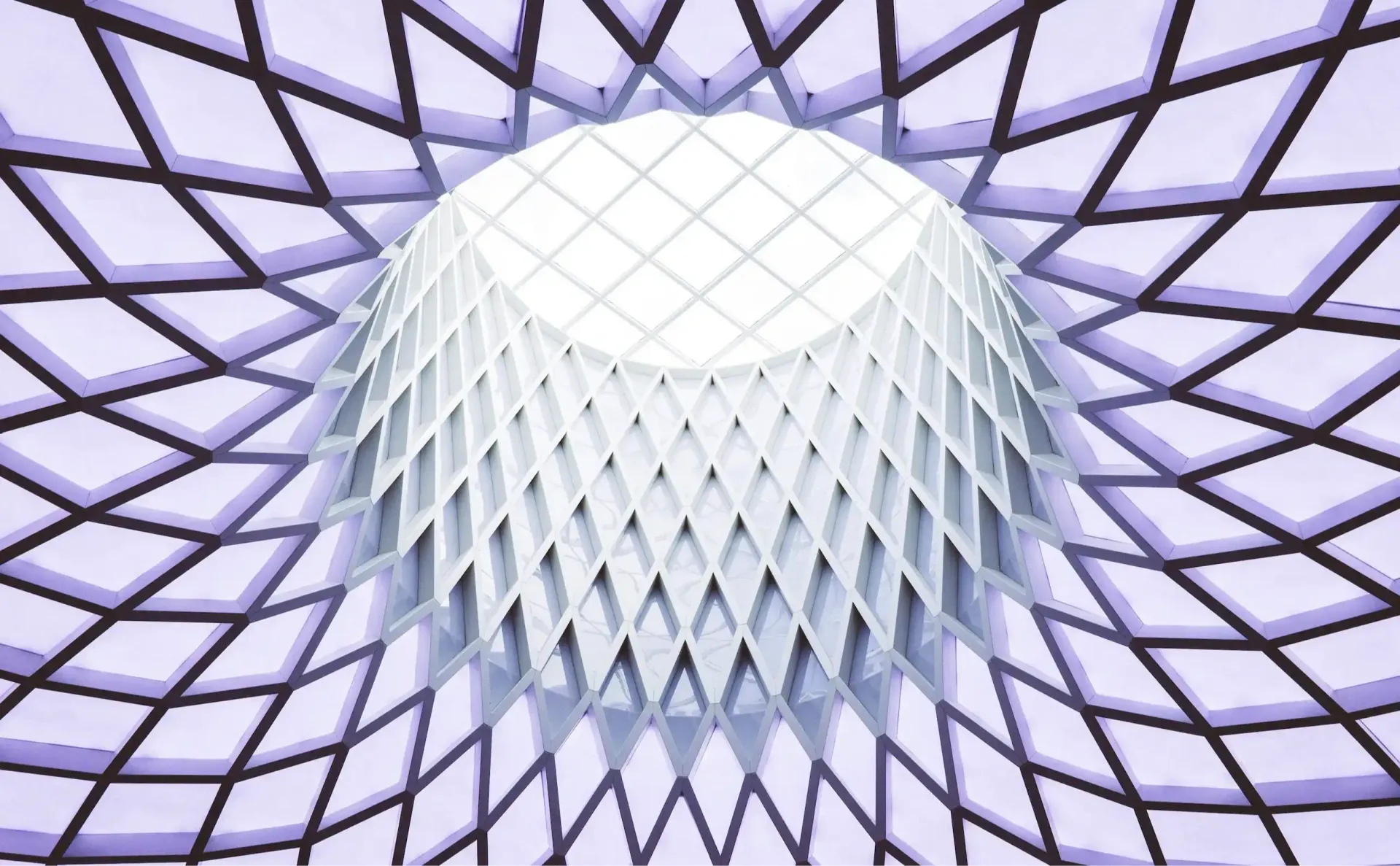 The underside of a lattice dome, hundreds of structural cells converging on a single bright aperture at the centre.