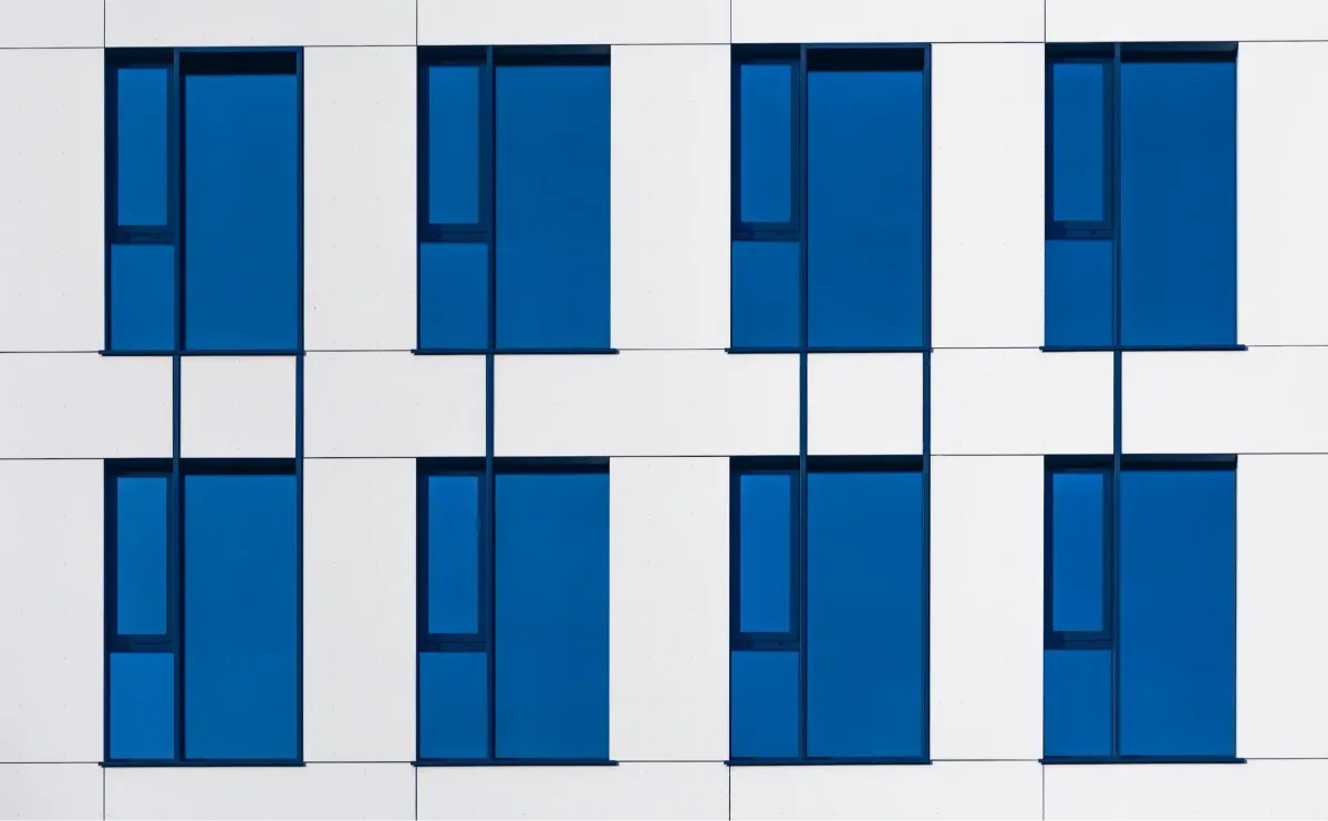 A white and blue building facade filled with rows of blue glass windows, seen straight on so the glazing reads as a continuous reflective surface.