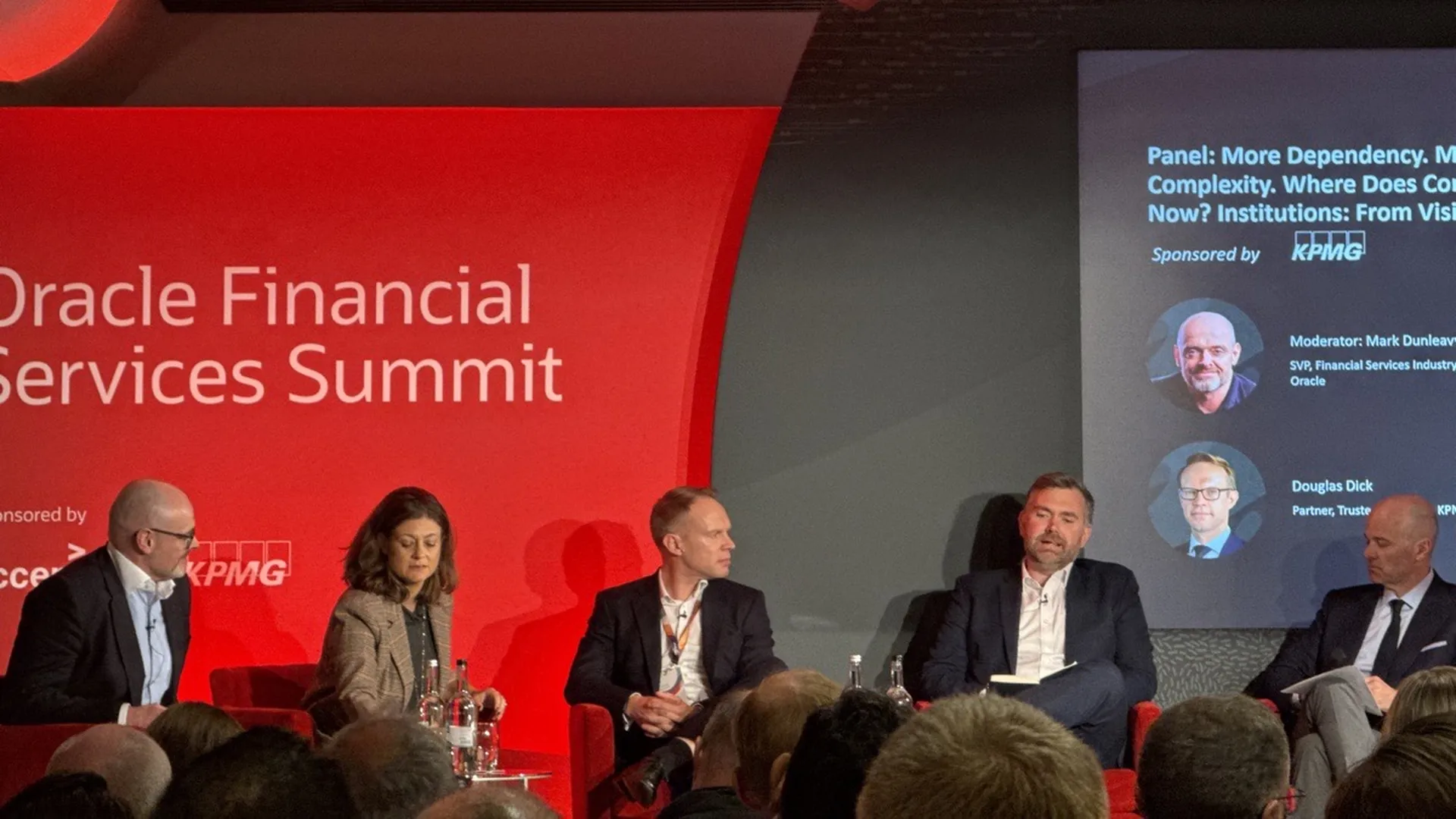 Cinco panelistas sentados en el escenario del Oracle Financial Services Summit, con la Dra. Leda Glyptis segunda por la izquierda y una pantalla que nombra al moderador, Mark Dunleavy de Oracle