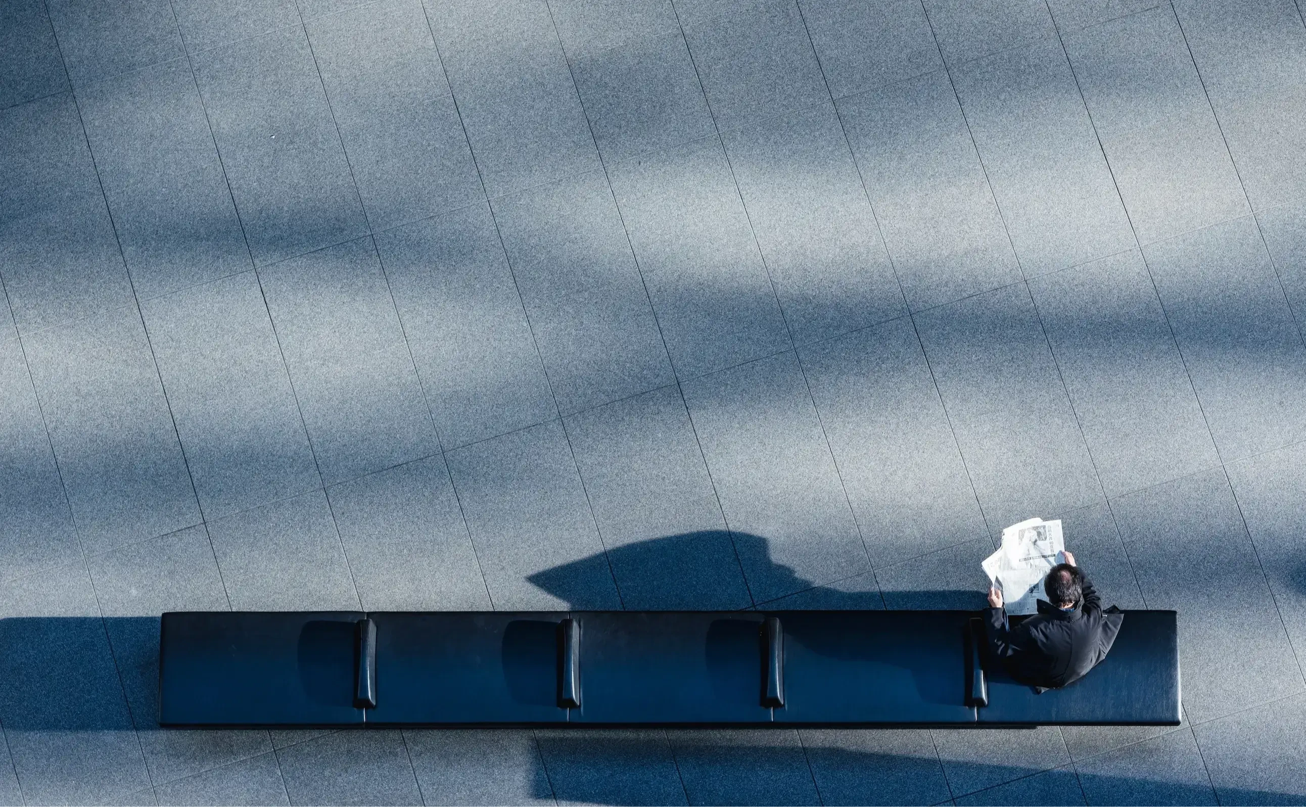 A person sitting on black bench reading newspaper
